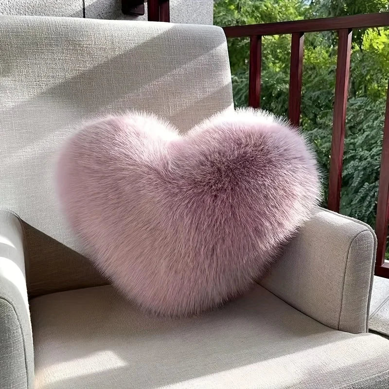 Heart-shaped fluffy pink pillow on a gray chair outdoors.