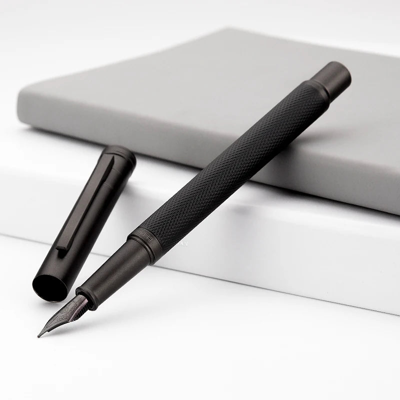Black fountain pen on a white surface with a gray notebook in the background