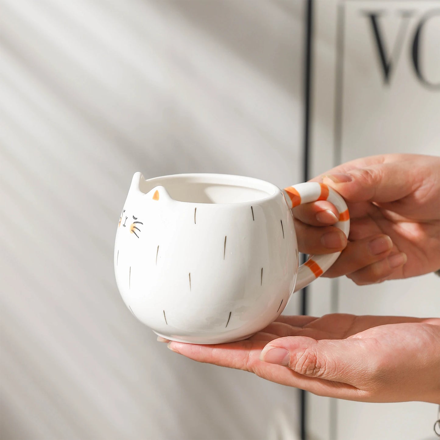 Person holding a white ceramic mug with orange accents and decorative patterns.