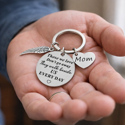 Keychain with heart-shaped 'Mom' charm and angel wing, held in a hand.
