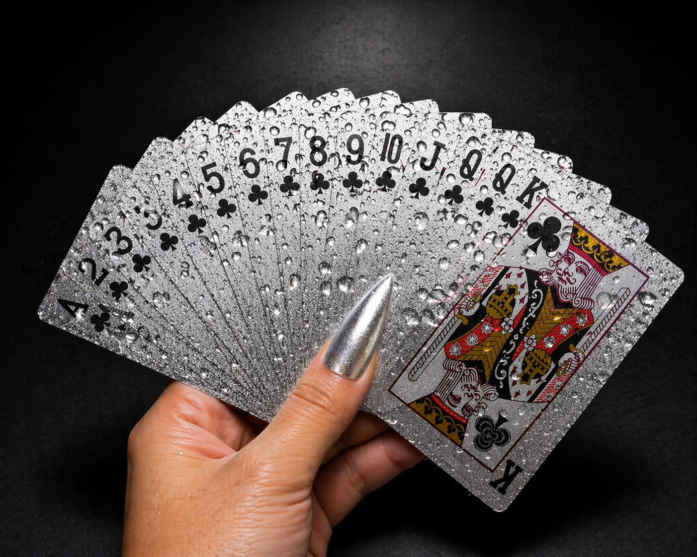 Hand holding a deck of silver playing cards against a black background
