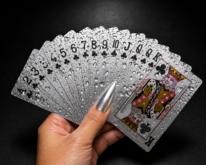 Hand holding a deck of silver playing cards against a black background