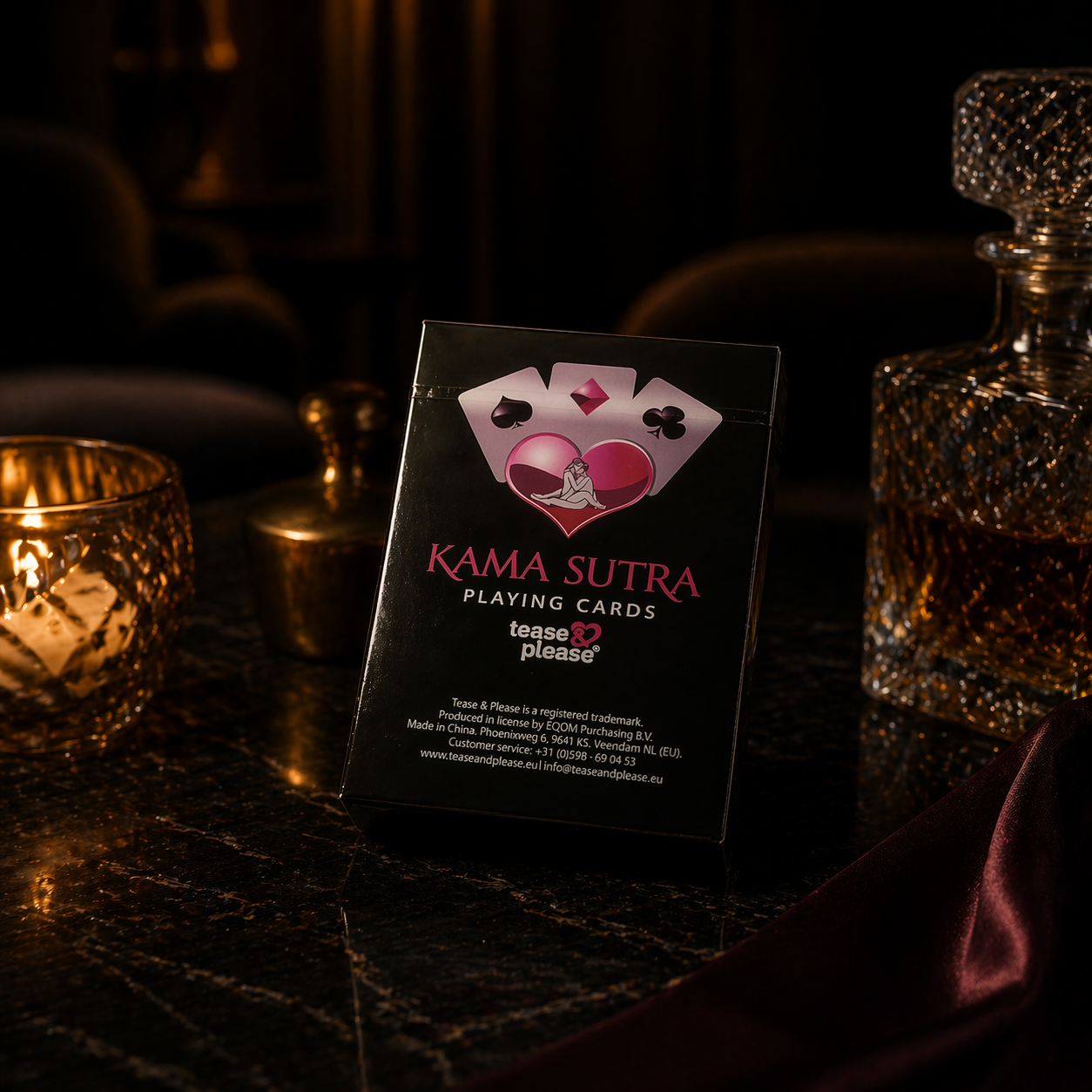 Kama Sutra playing cards packaging on a dark surface with candles and glasses in the background