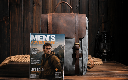 Brown leather backpack and 'Men's Adventures' magazine on a wooden surface with a dark wooden background.