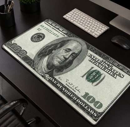 100-dollar bill design desk mat on a desk with office items.