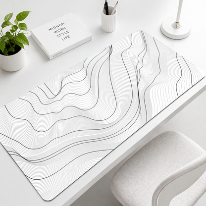 Desk setup with a decorative white mat featuring wavy lines, a plant, and a book.