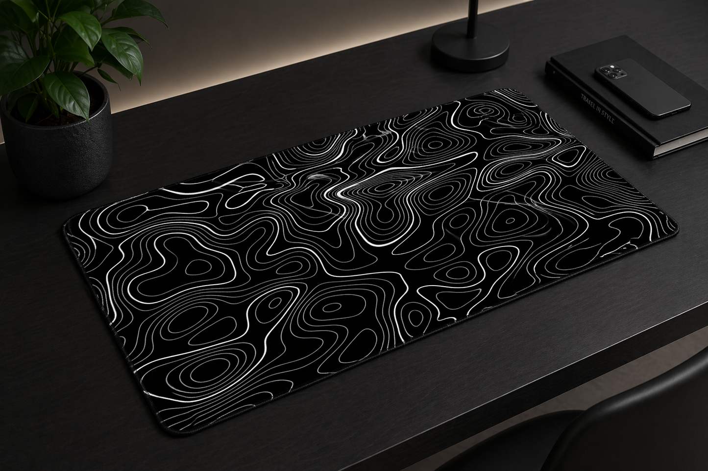 Black and white patterned mouse pad on a dark surface with a plant and notebook in the background.
