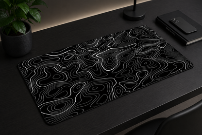 Black and white patterned mouse pad on a dark surface with a plant and notebook in the background.