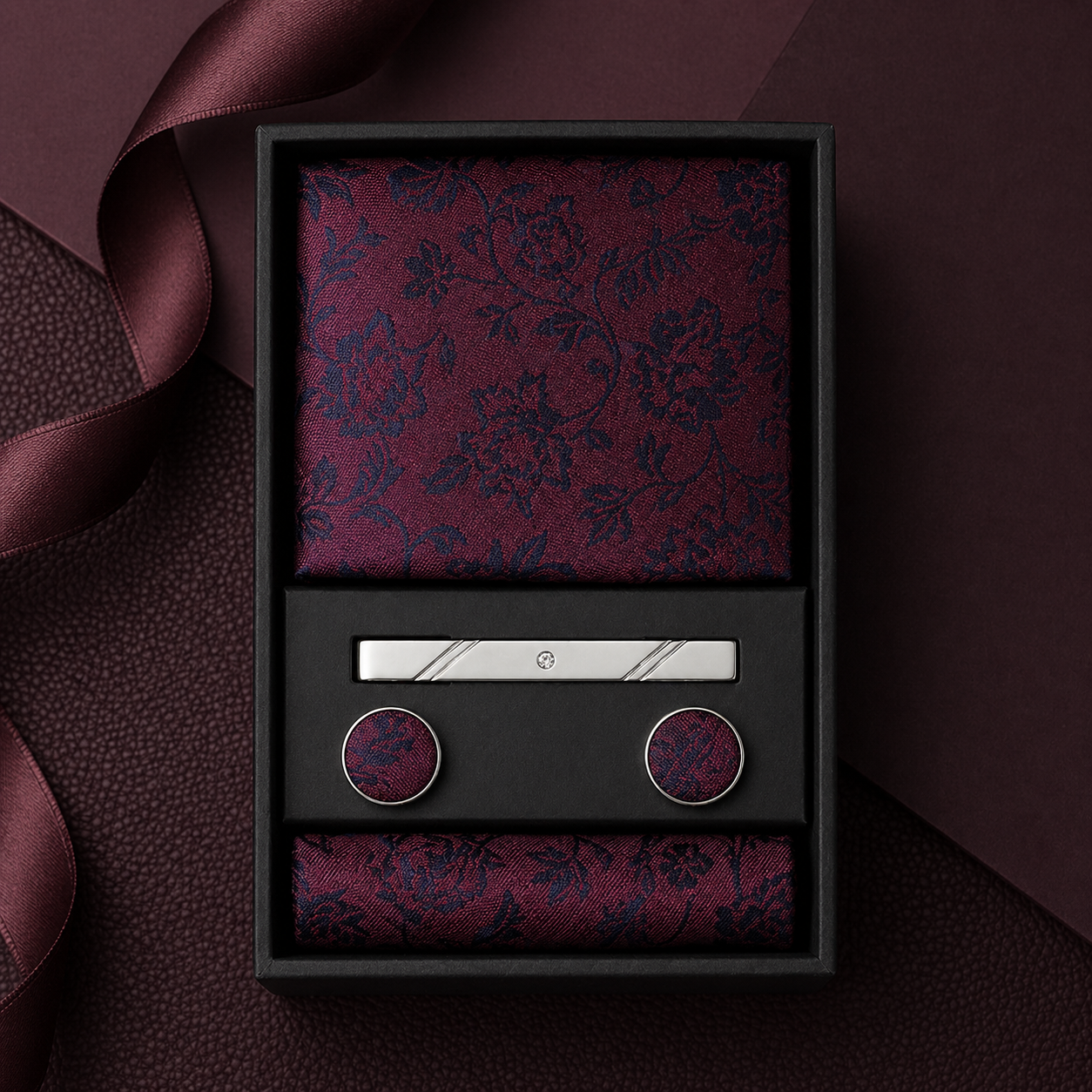 Maroon floral pocket square and cufflinks set in a black box on a dark background