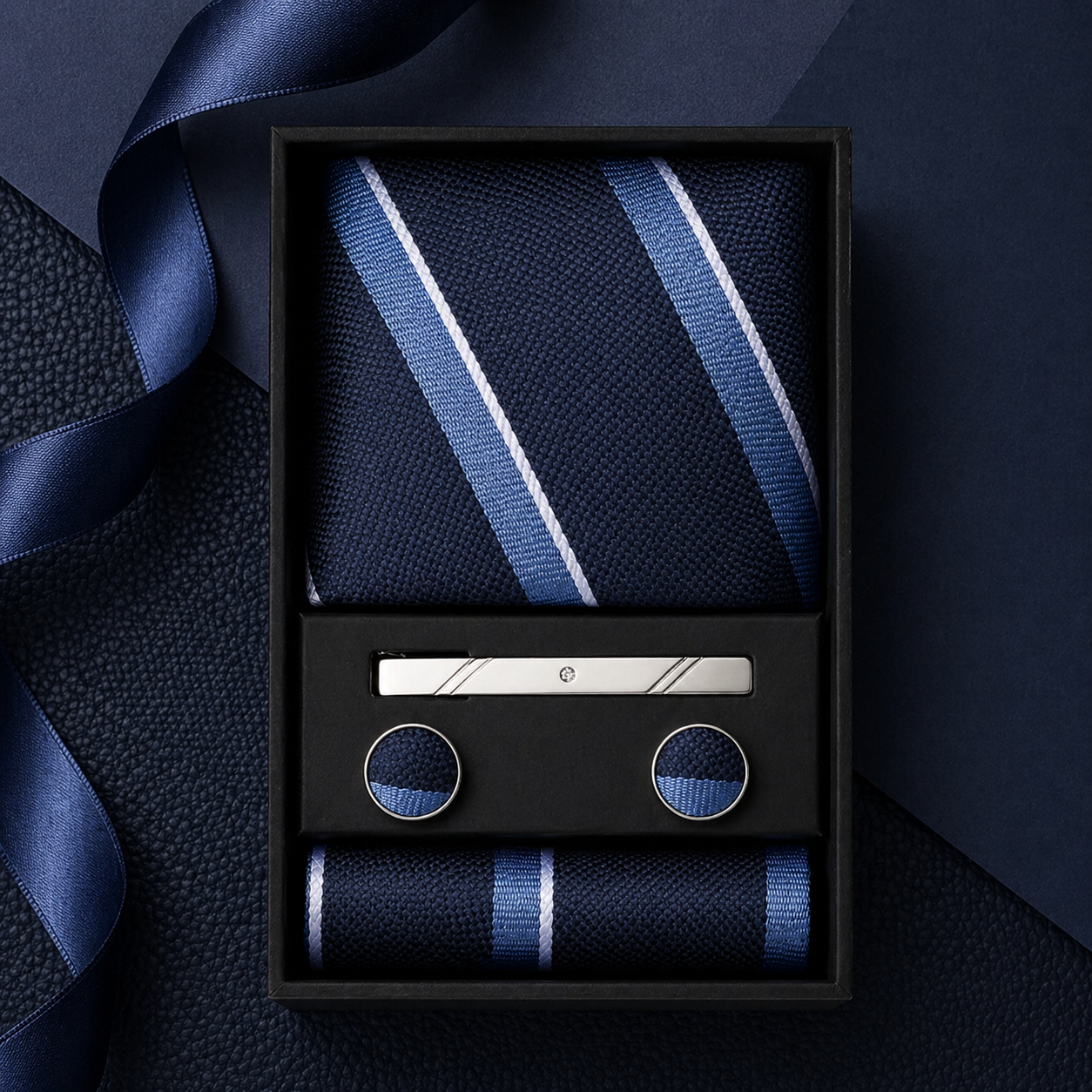 Navy blue tie with white stripes, cufflinks, and pocket square set in a black box on a dark background.