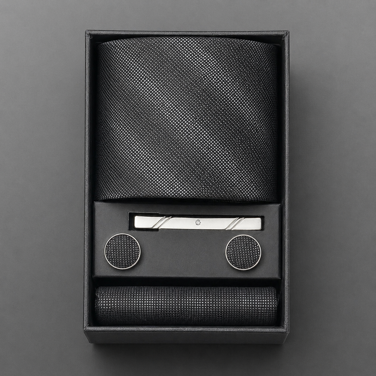 Black textured tie set with tie bar and tie clips in a box on a gray background