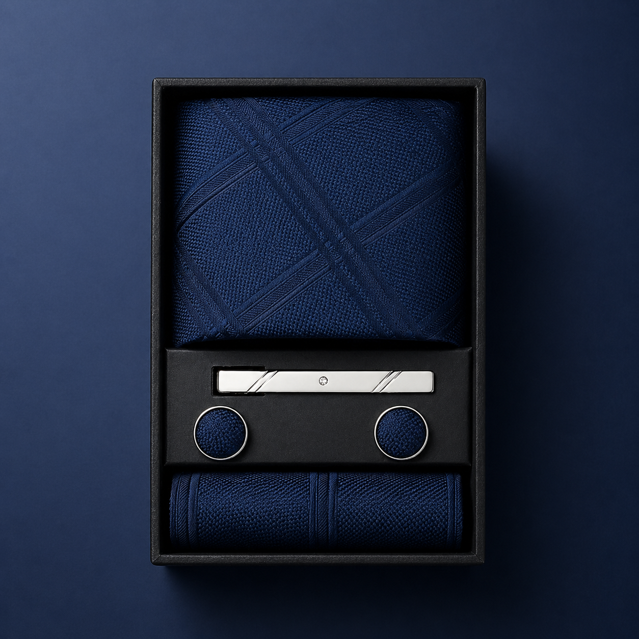 Set of blue fabric items including a towel, cufflinks, and a bar of soap in a black box on a dark blue background.