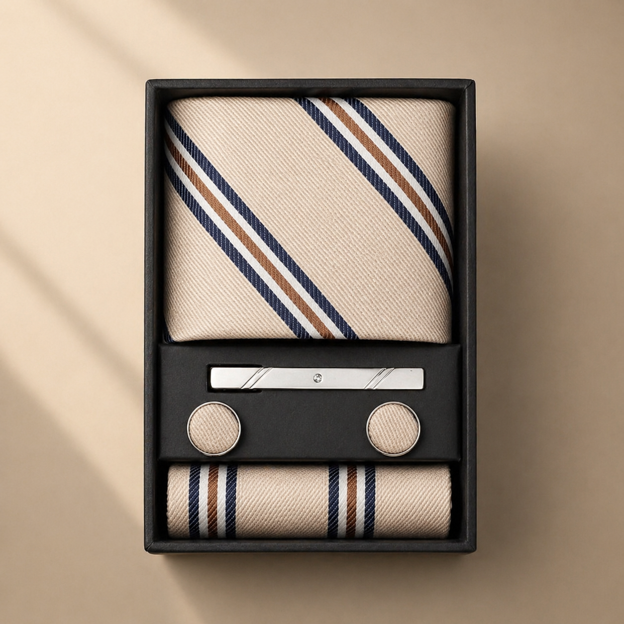 Tie set with striped tie, pocket square, and cufflinks in a black box on a beige background