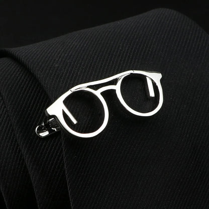 Silver eyeglasses-shaped lapel pin on a black textured fabric background
