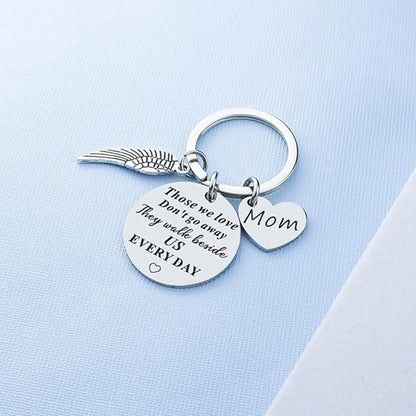 Silver keychain with angel wing, heart-shaped 'Mom' tag, and engraved message on a light blue background.