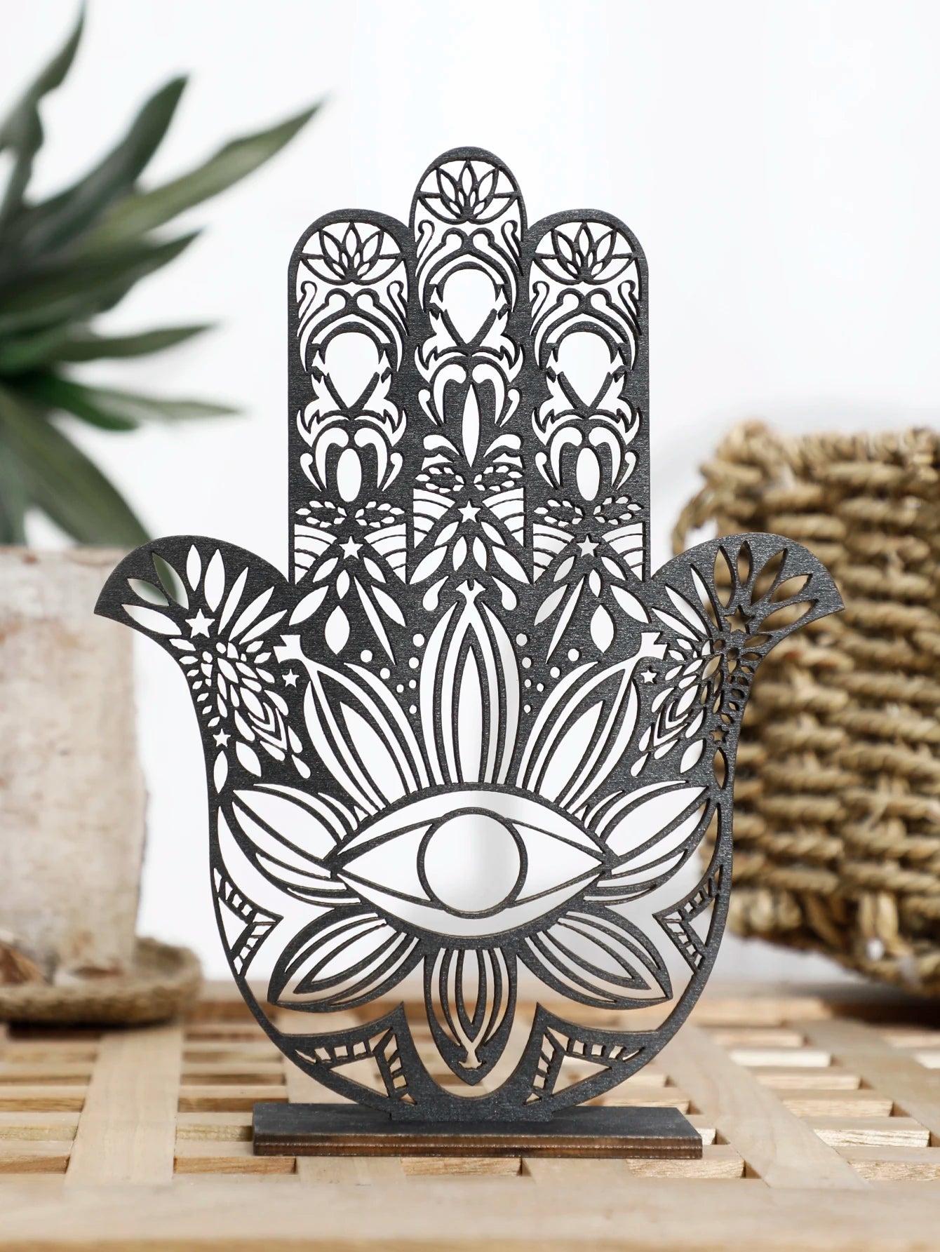 Decorative metal Hamsa hand with intricate patterns on a wooden stand.
