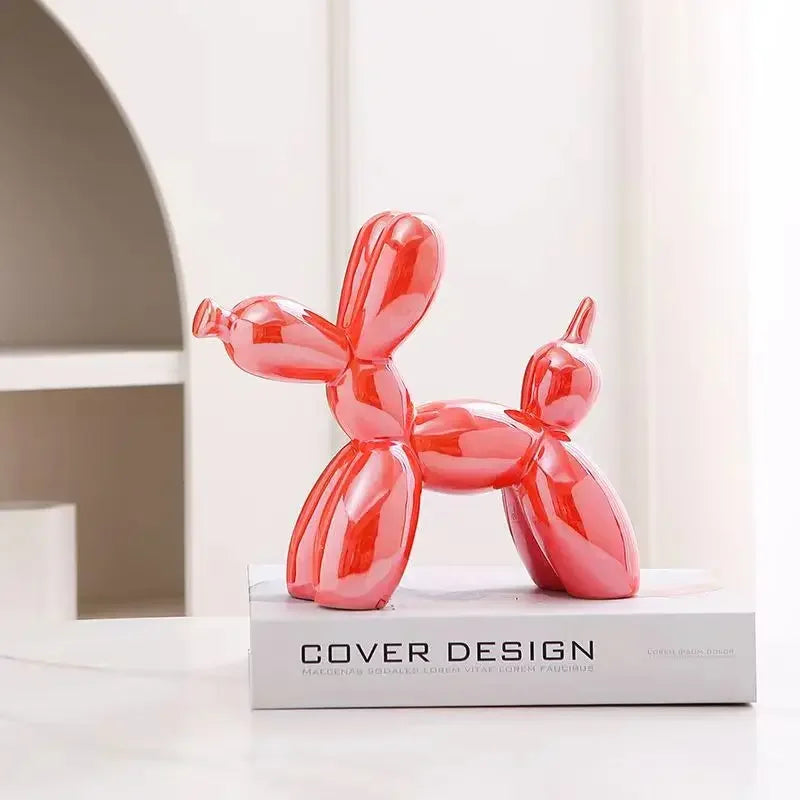 Red balloon dog sculpture on a white surface with a book titled 'Cover Design' in the background.