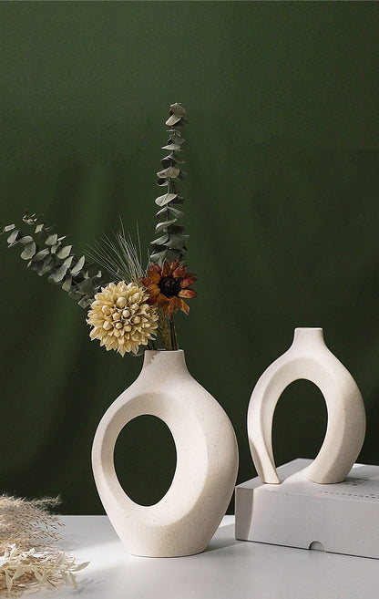 Two white ceramic vases with circular designs on a dark green background