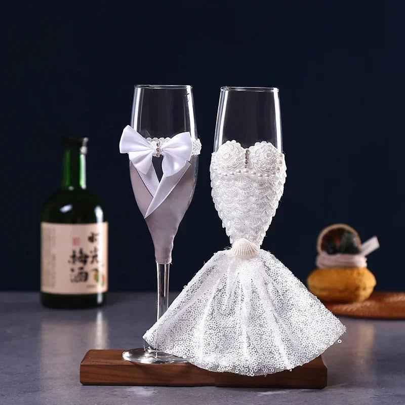 Two decorative champagne flutes shaped like a bride and groom on a wooden base with a dark background.