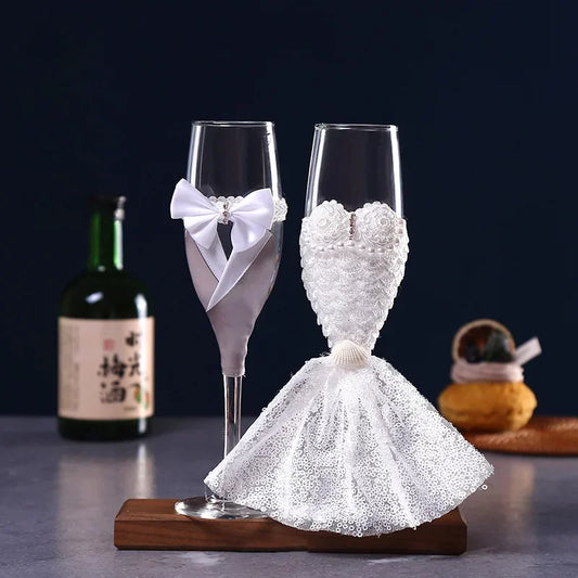 Two decorative champagne flutes shaped like a bride and groom on a wooden base with a dark background.