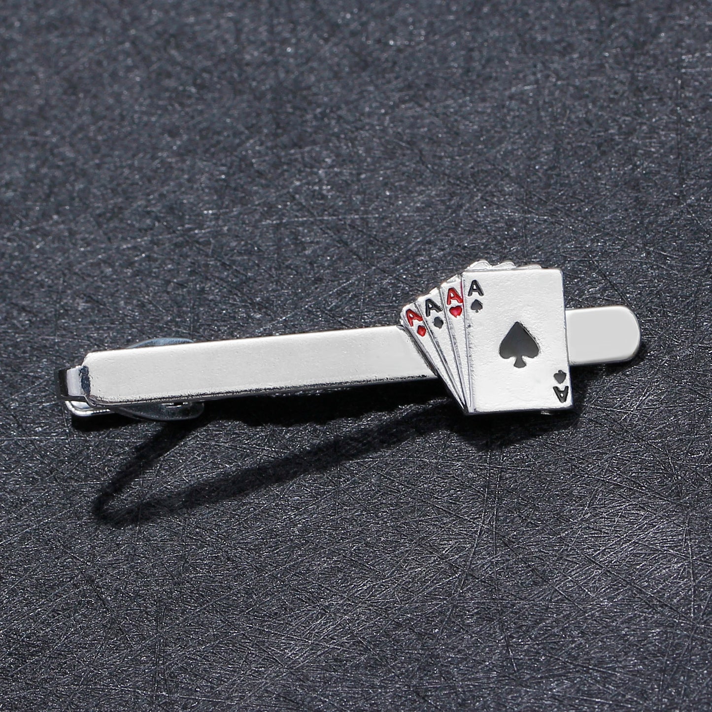 Silver tie clip with playing card design on a dark textured background