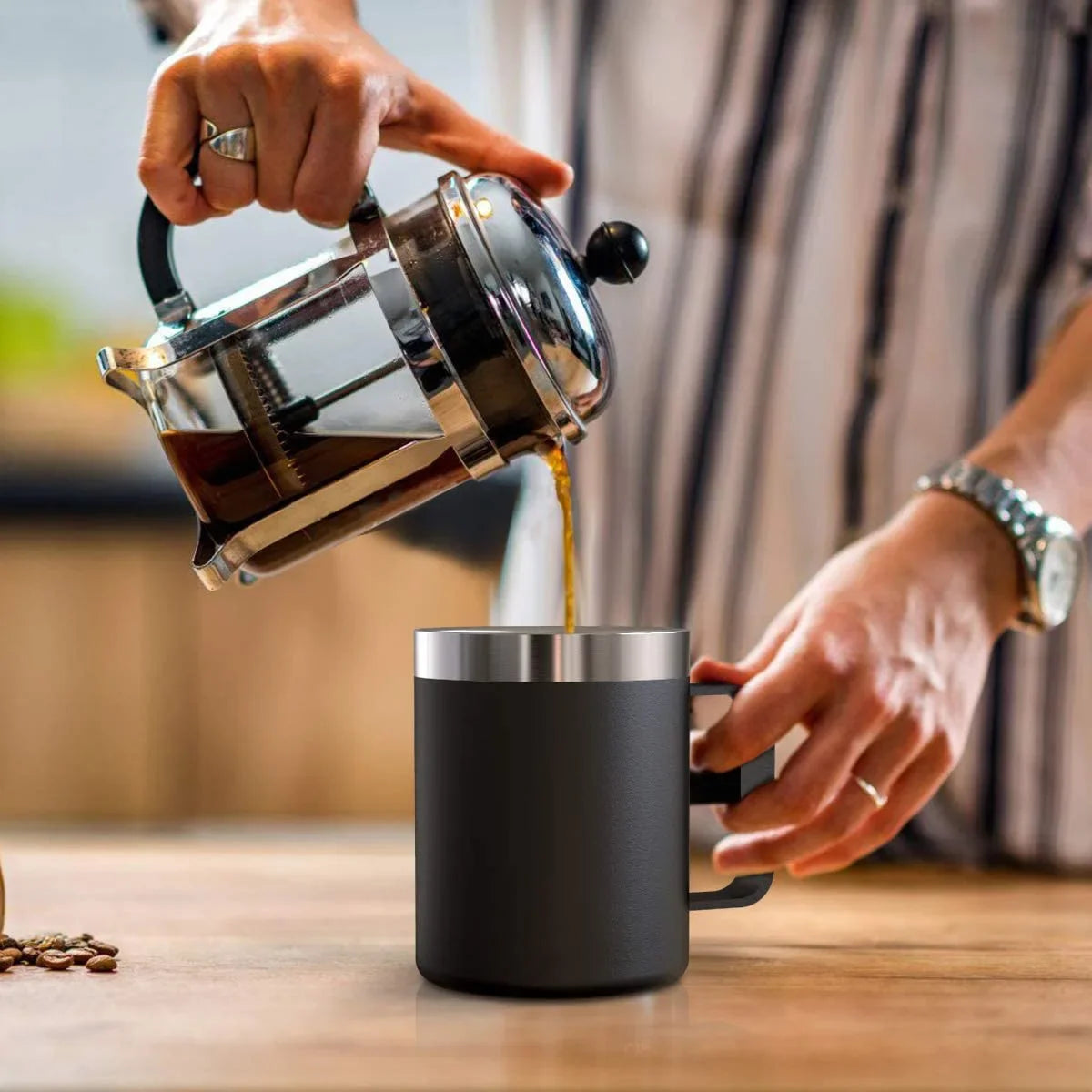 Person pouring coffee from a French press into a black mug on a wooden table.
