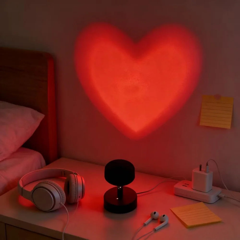 Heart-shaped light projection on a wall with headphones and other items on a desk.