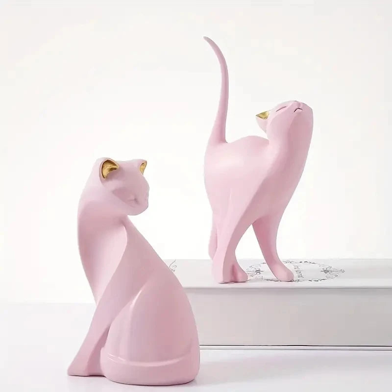 Two pink cat figurines with gold accents on a white surface.
