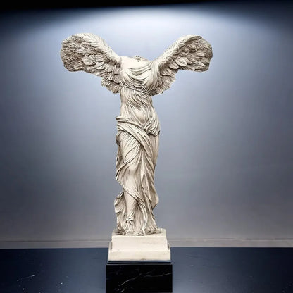 Statue of a winged figure on a dark base against a gray background