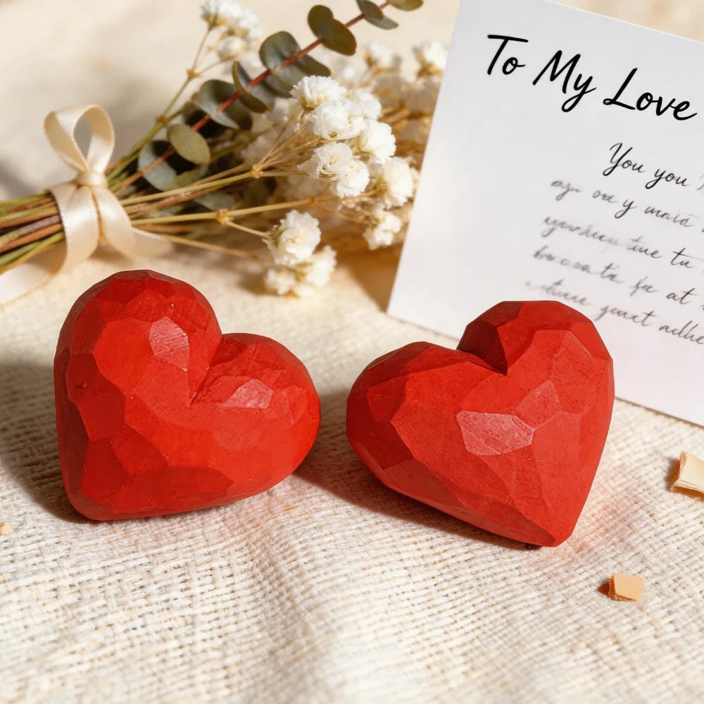 Two red heart-shaped objects on a textured surface with a card and flowers in the background.