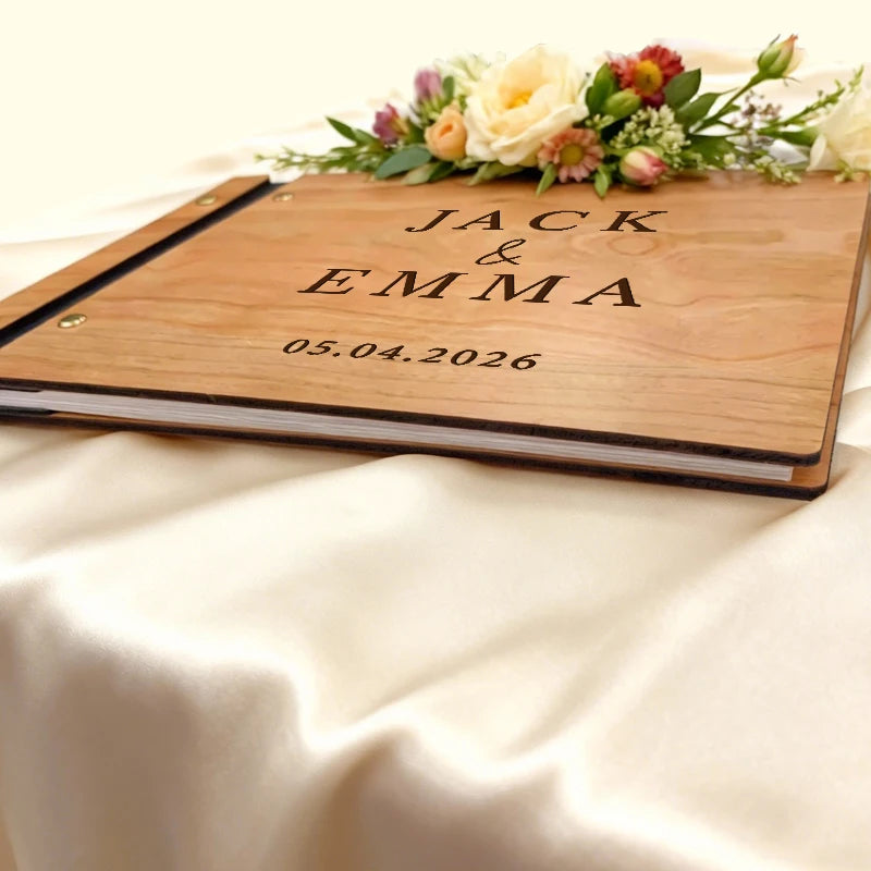 Wooden album with 'JACK & EMMA' and a date, decorated with flowers on a white fabric background.