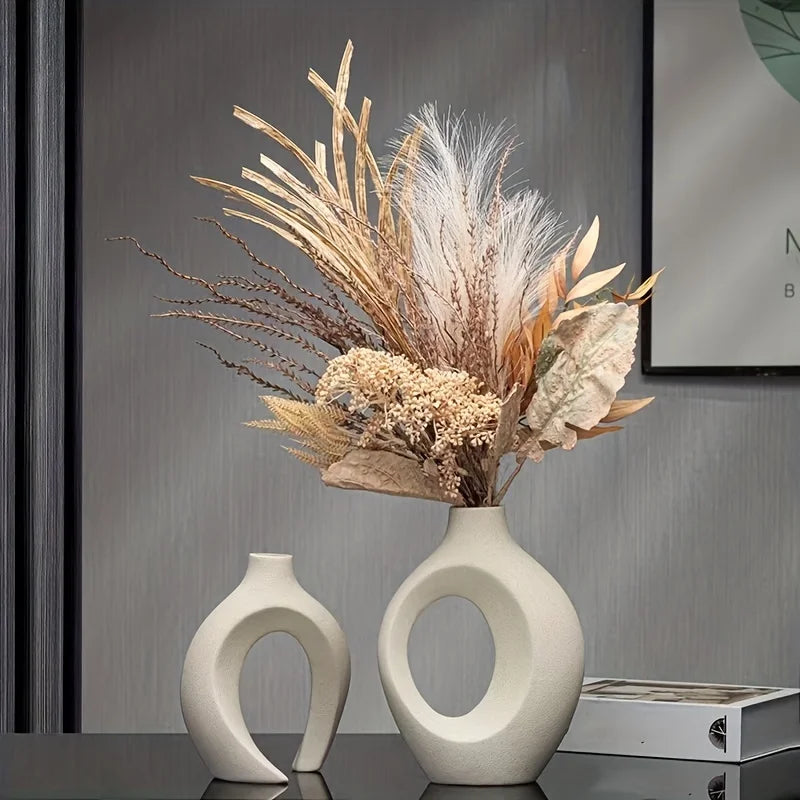 Two white ceramic vases with dried plants on a dark surface.