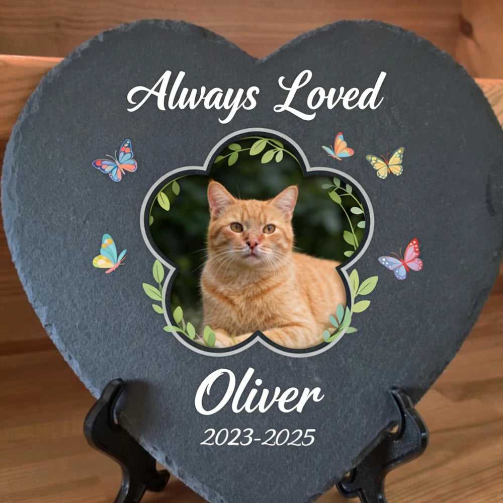 Heart-shaped slate plaque with a cat photo, 'Always Loved Oliver 2023-2025' text, and butterflies on a wooden background.