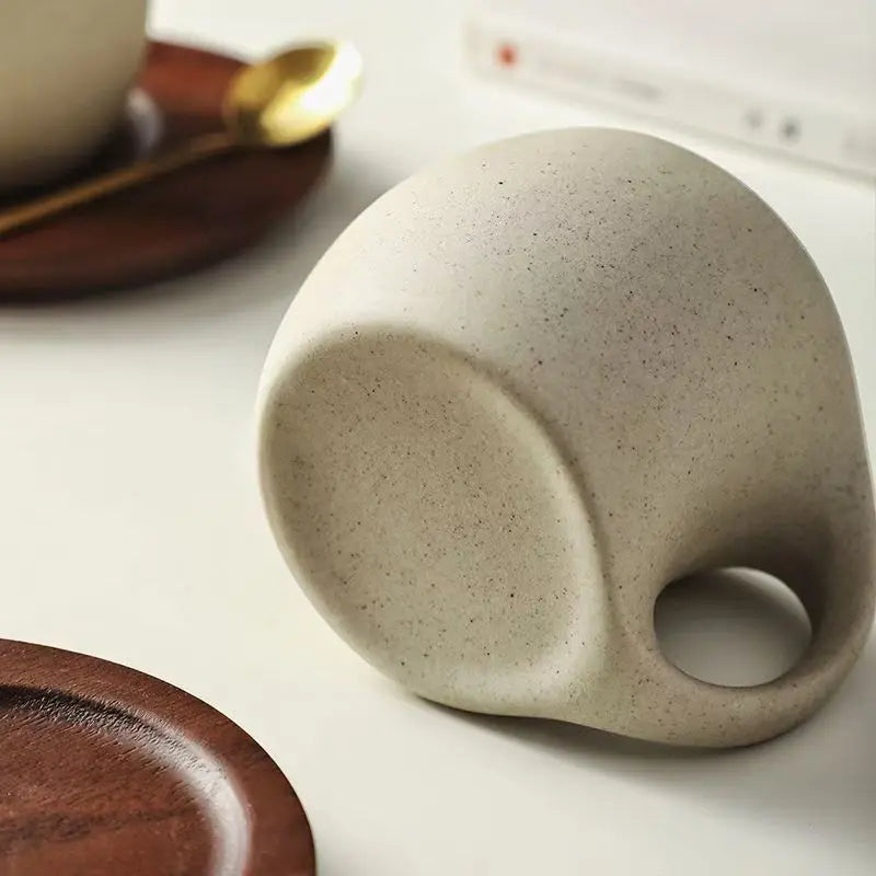 Speckled ceramic mug on a white surface with wooden coaster and cup in the background