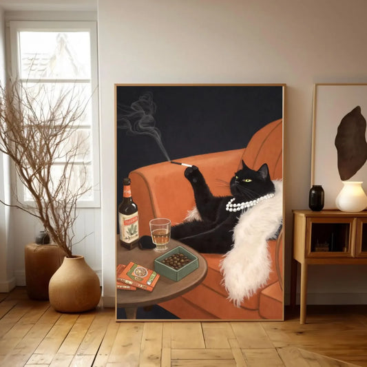 Framed artwork of a black cat lounging on an orange couch with a drink and books in a room with wooden flooring and a window.