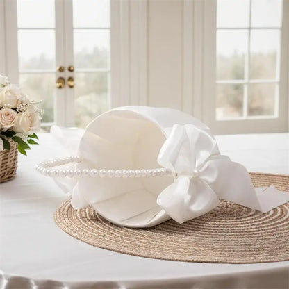 White sun hat with a large bow and pearl details on a table with a blurred background