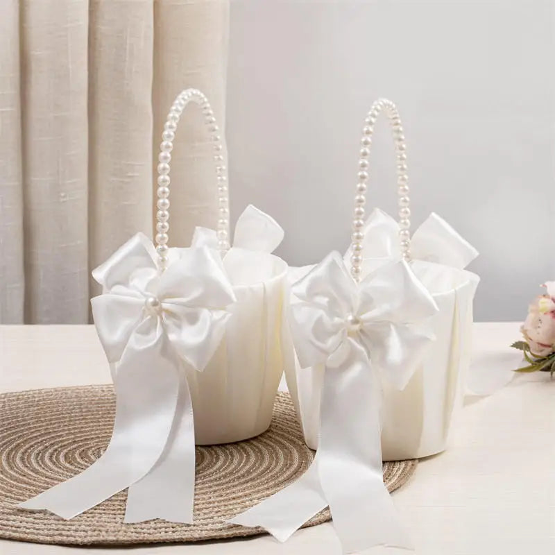 Two white flower girl baskets with pearl handles and large white bows on a neutral background.