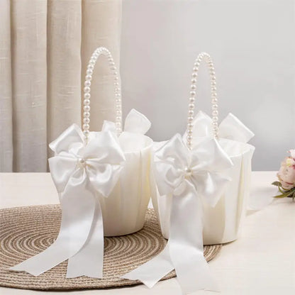 Two white flower girl baskets with pearl handles and large white bows on a neutral background.