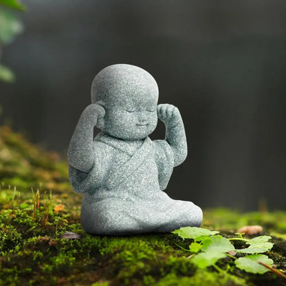 Stone statue of a child in a meditative pose on a mossy surface