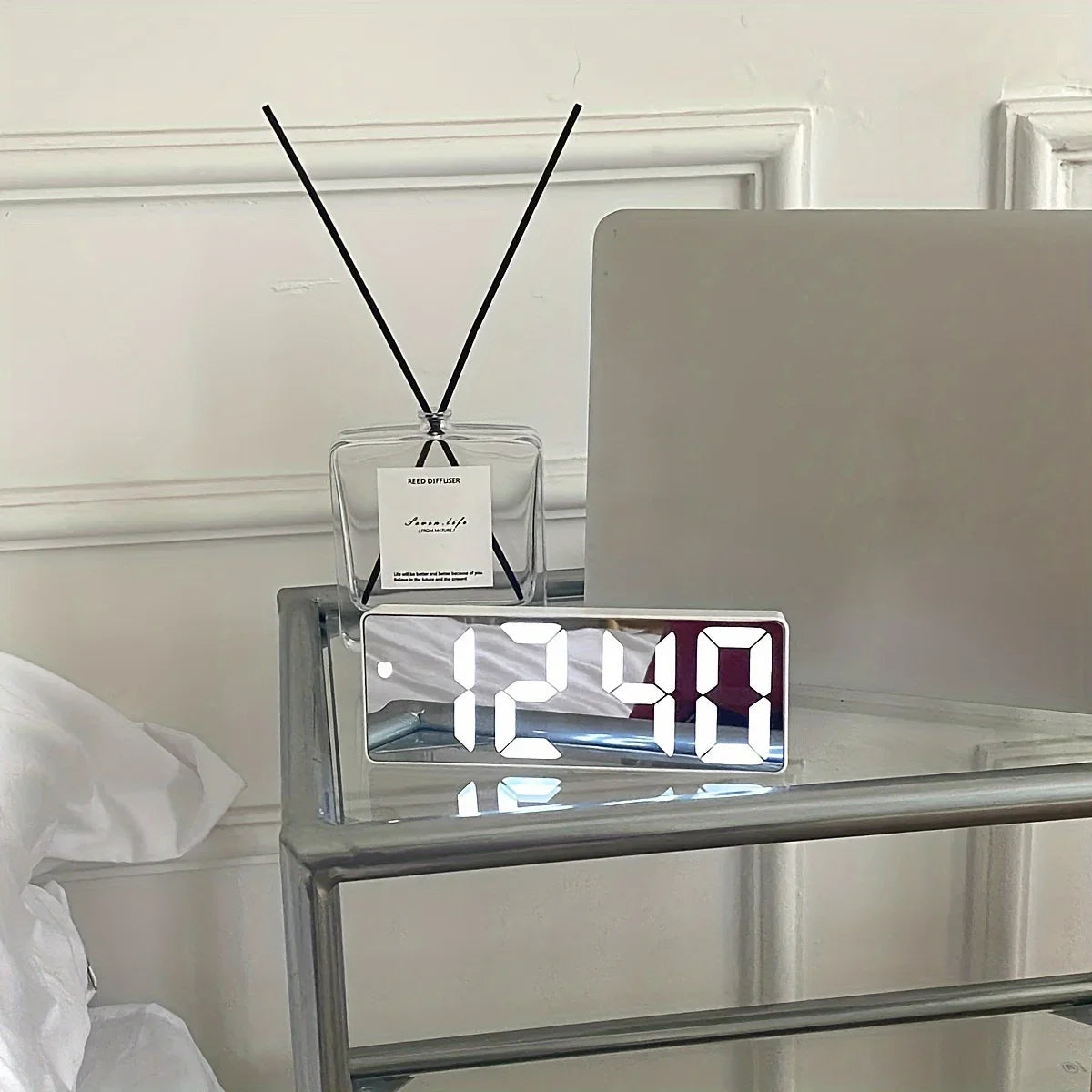 Digital clock on a nightstand next to a bed with a white pillow