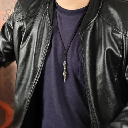 Person wearing a black leather jacket over a dark shirt with a necklace featuring a decorative pendant.