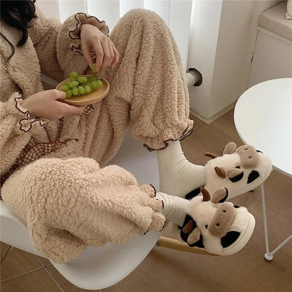Person wearing fluffy pajamas and cow-themed slippers, sitting on a chair with a bowl of grapes.