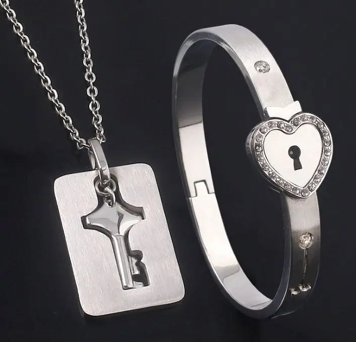 Silver key pendant necklace and heart-shaped lock bracelet on a dark background