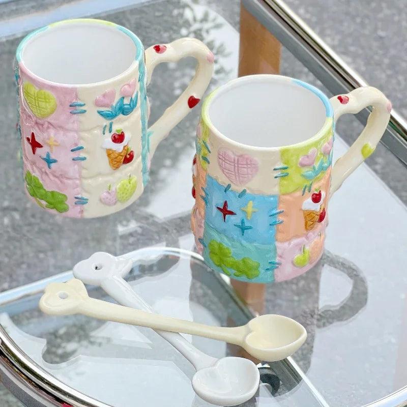 Two colorful ceramic mugs with decorative patterns on a glass surface, accompanied by a white spoon.