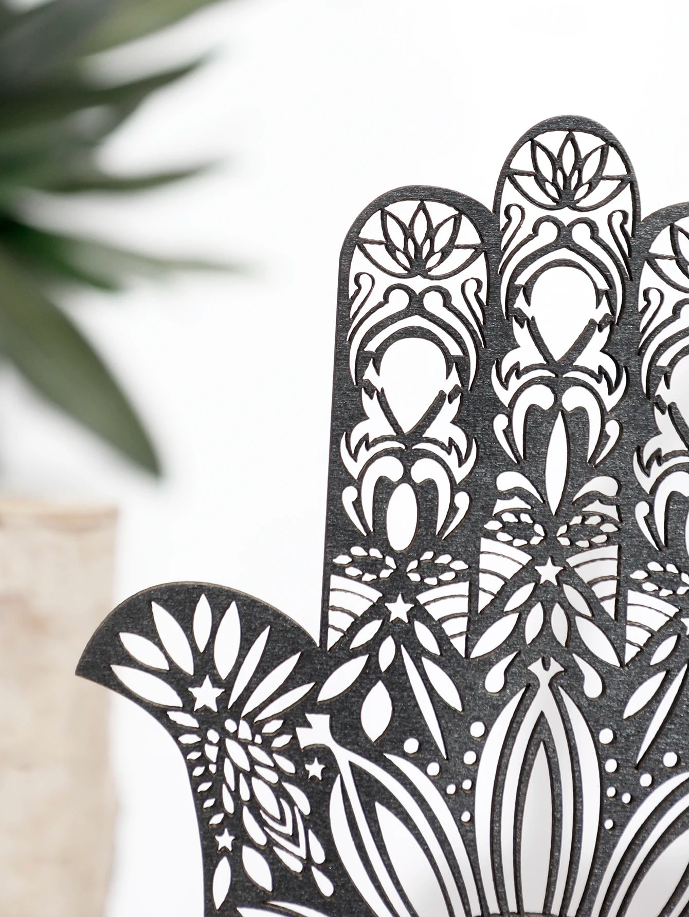 Decorative black Hamsa hand with intricate patterns against a blurred natural background