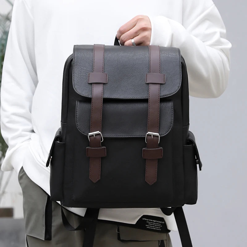 Gray backpack with brown straps held by a person wearing a white shirt.