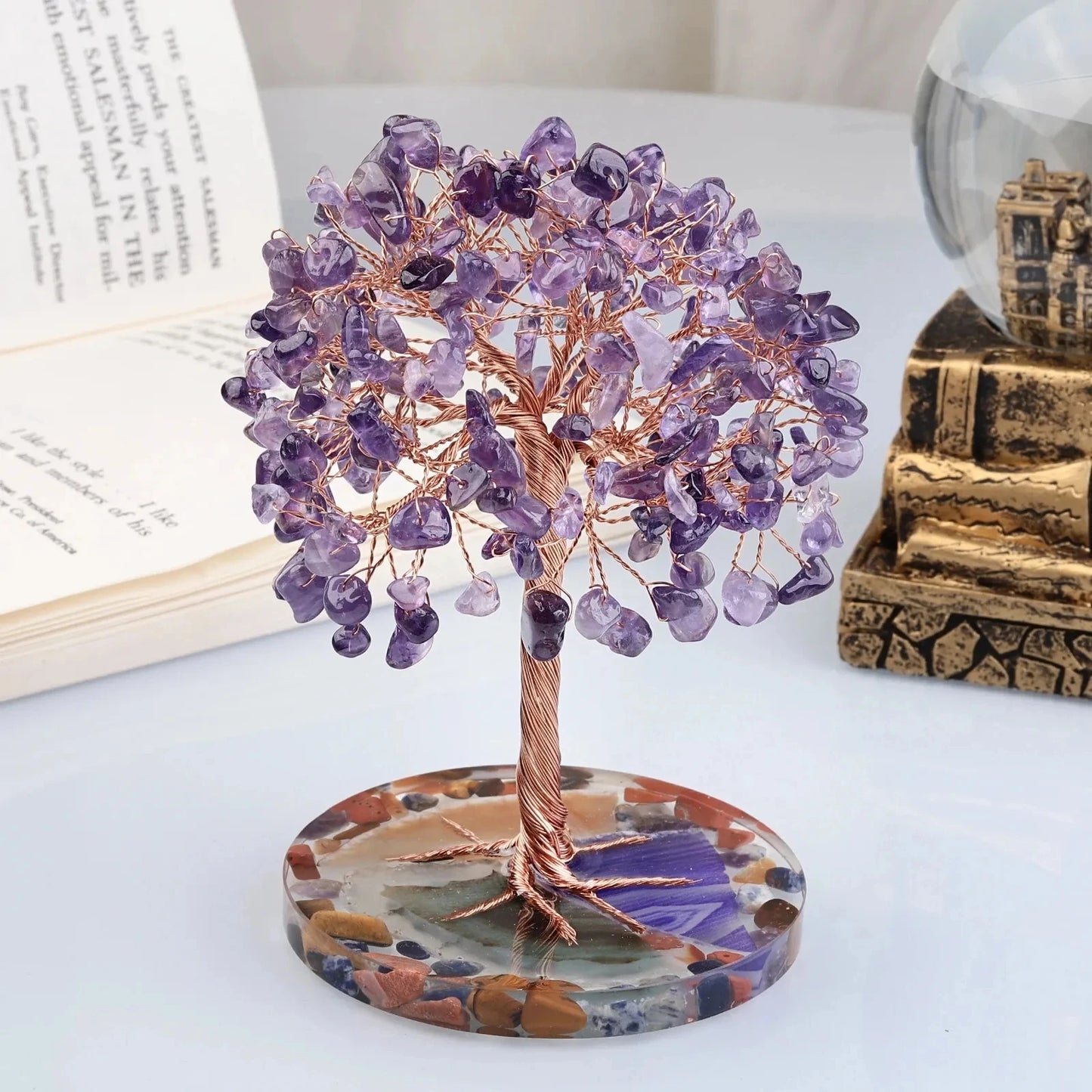 Decorative crystal tree on a round base with a book and decorative box in the background.