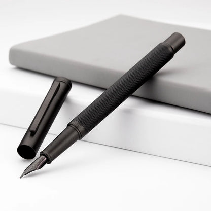 Black fountain pen on a white surface with a gray notebook in the background