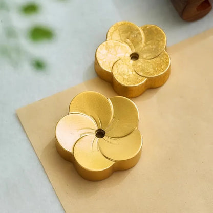 Two gold flower-shaped candles on a beige surface with a blurred green background