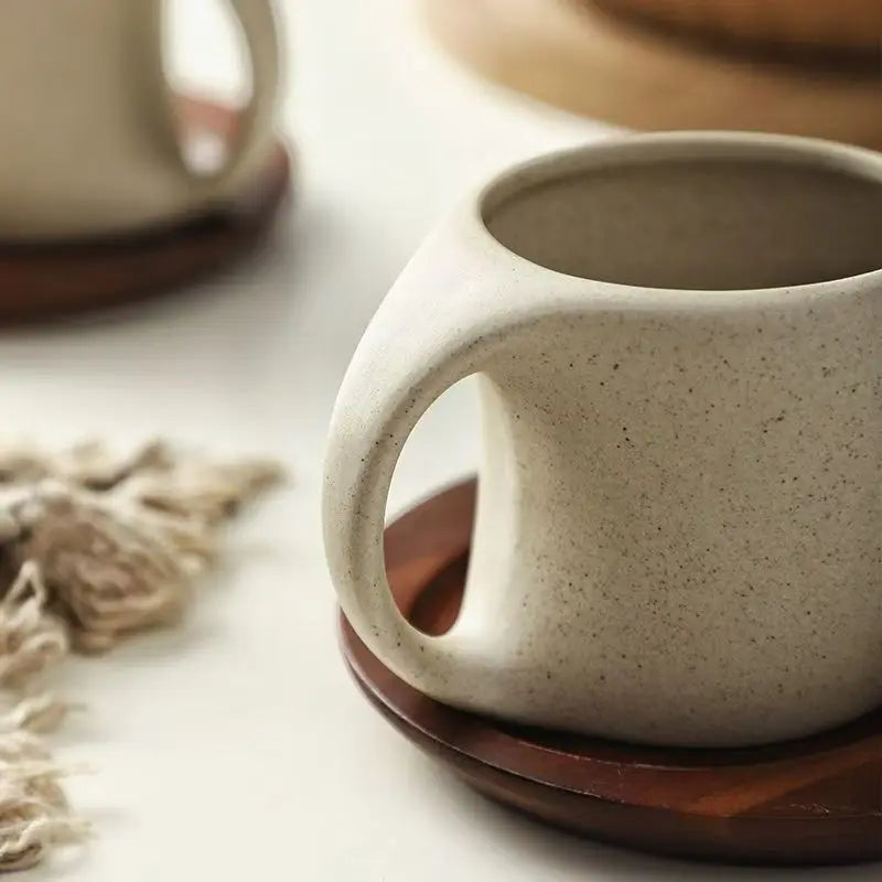 Close-up of a ceramic mug with a wooden coaster on a light surface.